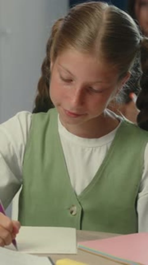 Young Girl Studies and Writes on Paper in Classroom