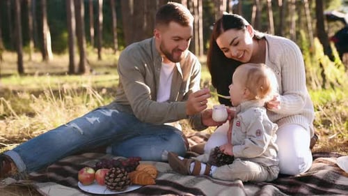 Feeding boy with child food. Family of father, mother and little son is outdoors in the forest