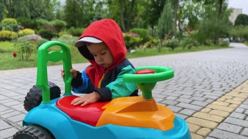 Adorable Caucasian toddler wearing jacket plays with toy car in the park.