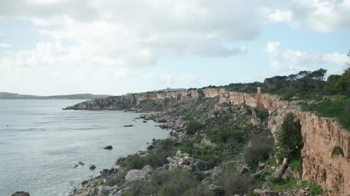 AERIAL: Steep Coastline in Mellieha Bay with Sharp Limestone Rocks at the Bottom of Shore