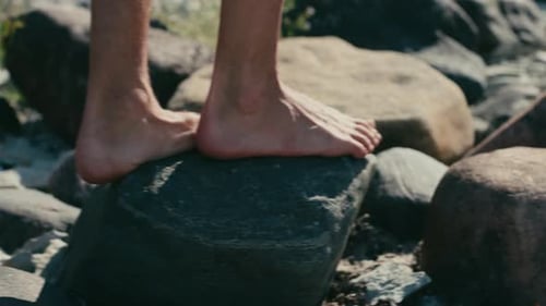 Man walking barefoot on rocks close to beach, close-up