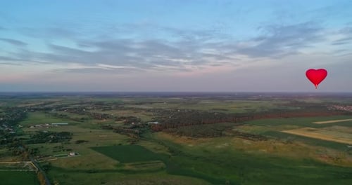 Red Heart Balloon Soaring over Rural Landscape