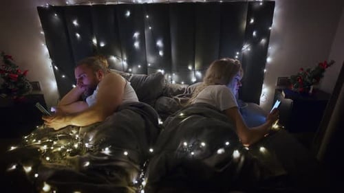 Couple in Bed, Looking at Phones at Night
