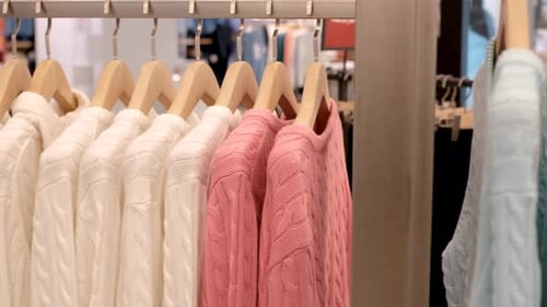 Knitted sweaters in pastel colors hang on wooden hangers in clothing store.