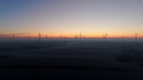 Silhouettierte Windturbinen auf nebligen Feldern bei Sonnenaufgang. - Luftaufnahme