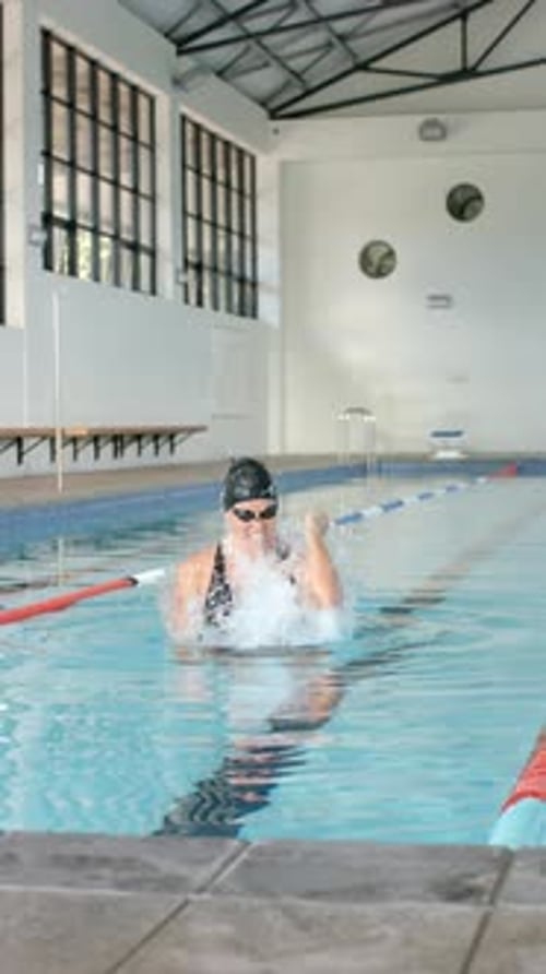 Vertical video: Swimming in indoor pool, woman celebrating victory with raised fist