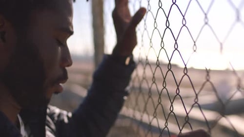 Man Gripping Fence in Urban Setting