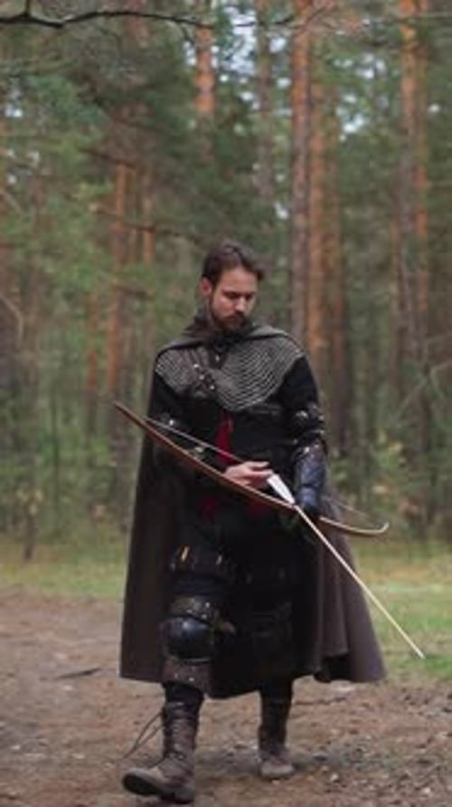 Man Wearing Costume of Medieval Warrior with Bow in Forest