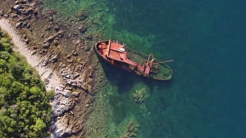 Altes kaputtes Schiff, halb versunken am seichten blauen Wasserufer, von oben nach unten