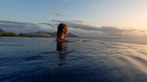 Mujer joven al atardecer en la piscina infinita al borde del abismo