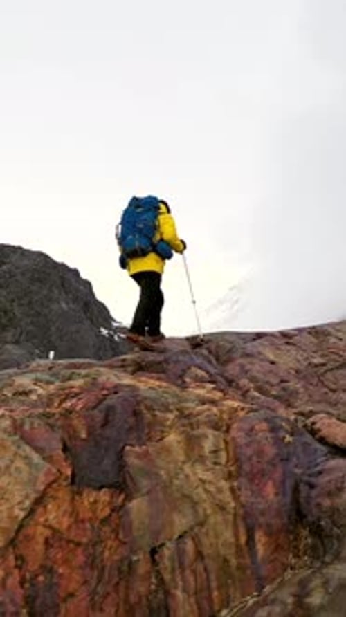 Mountaineer Walking on Snow with Trekking Poles Near Snowy Mountain Range