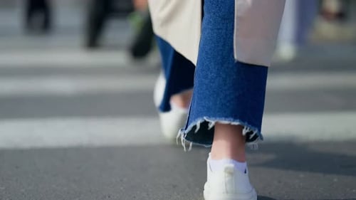 Walking in jeans and white sneakers on crosswalk