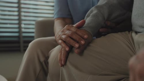 Nahaufnahme der Hand einer älteren Frau, die tröstet, während sie die Hand eines älteren Mannes hält