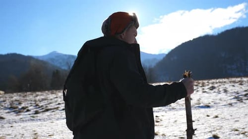 Young Hiker Goes Nordic Walking with Sticks on Snowy Field at Mountain Background