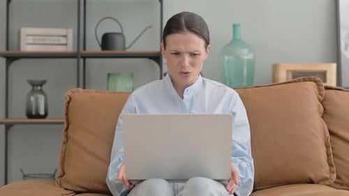 Woman Shocked by Loss on Laptop while Sitting on Sofa