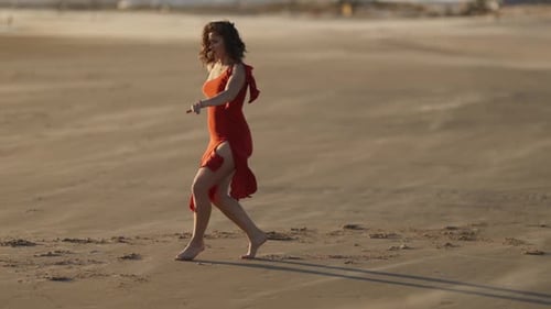 Graceful Smiling Young Woman in Red Dress Dancing on Sandy Beach in the Wind