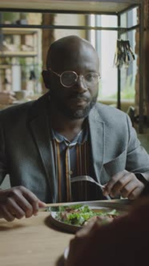 Businessman Eating Lunch and Talking with Colleague in Cafe