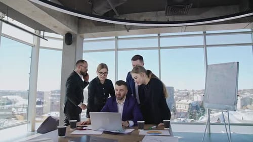 Group of colleagues stand around the boss with a laptop.