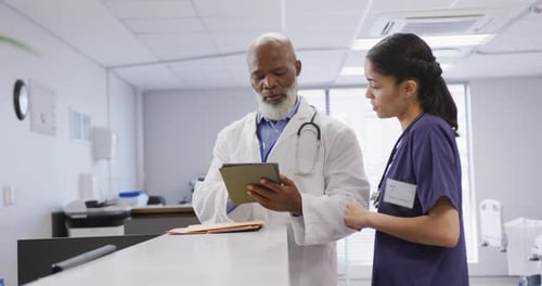 Diverse male and female doctors using tablet and talking at hospital