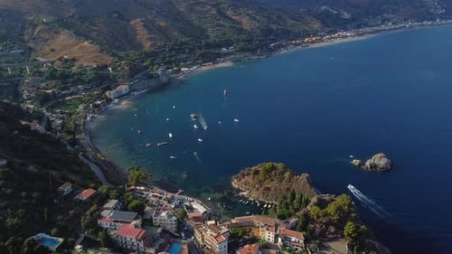 Circular aerial drone shot of Italian coastline, in Taormina, Sicily, with boats cruising in the bay