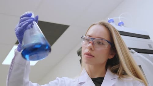 Technicien de laboratoire analysant une solution chimique bleue dans un flacon Erlenmeyer au laboratoire