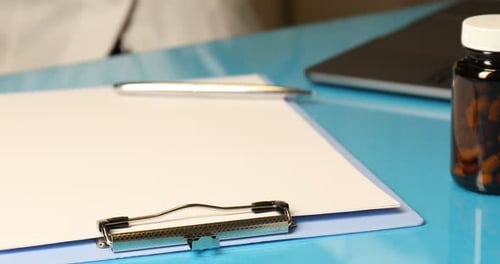 Doctor Writing on Clipboard at Desk with Stethoscope