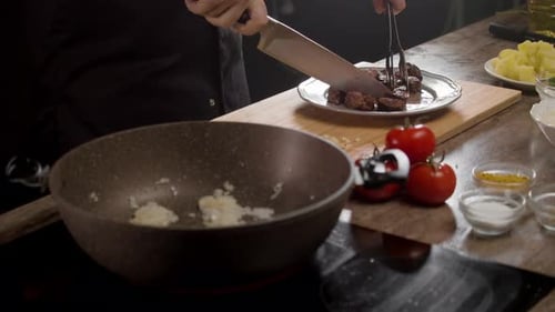 A Chef in a Black Uniform is Cooking Meat Dishes in the Restaurant's Kitchen
