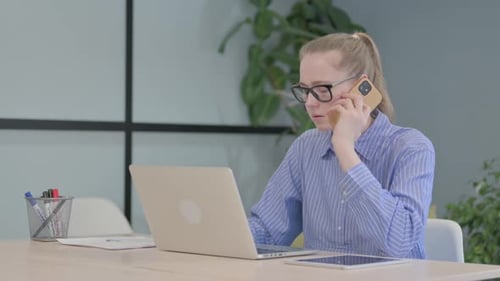 Young Woman Working at Laptop Talking on Phone