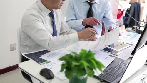 Two Businessmen Reviewing Financial Documents and Discussing Strategy in Office