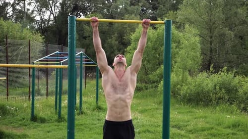 Athletic Man Trains Abdominal Muscles Raising Legs on Horizontal Bar at Sports Ground Young