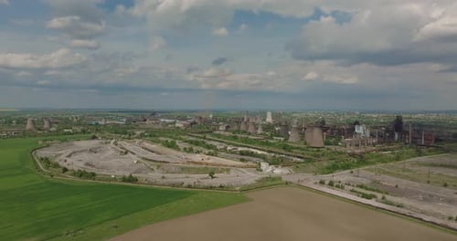 Old industrial complex showing multiple smokestacks surrounded by agricultural fields, on a sunny cl
