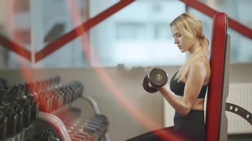 Pretty blonde fitness trainer practicing dumbbell exercises in a gym workout
