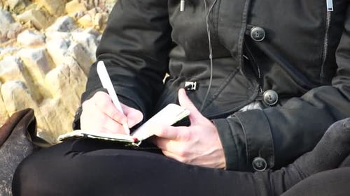 Woman Writing in a Notebook on Rocky Beach