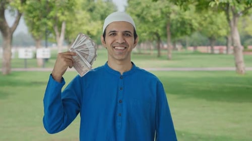 Happy Muslim man using money as fan in park