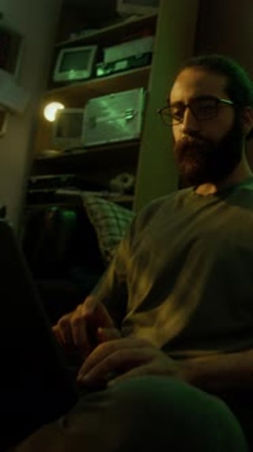 Bärtiger Mann arbeitet an seinem Laptop, während er auf dem Boden sitzt und sich auf die Couch lehnt