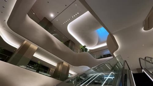 A sleek modern interior with curved architecture and escalators under soft ambient lighting