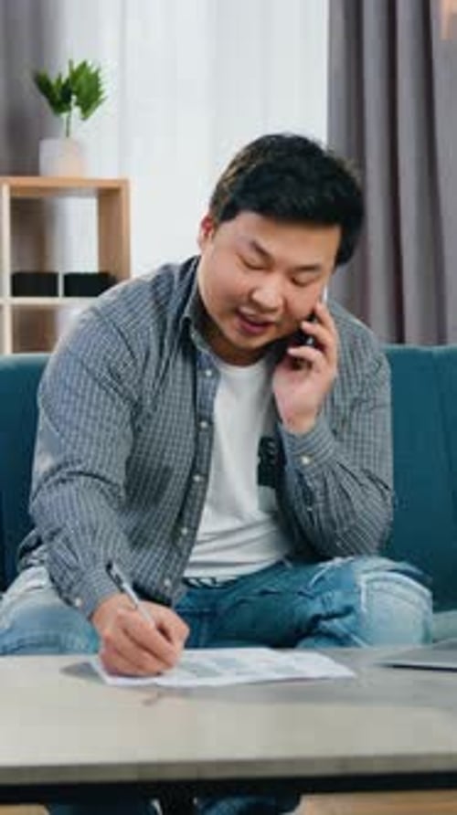 Attractive in Good Mood Confident Adult Asian Man Talking on Smartphone and Writing Important Notes