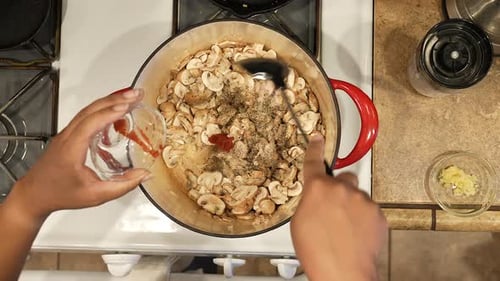 Adding salt, pepper and bay leaves to sauteed mushrooms for an organic, Vegan soup recipe - overhead