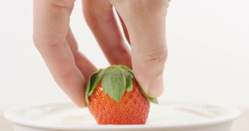 Macro shot of a hand dipping the natural and organic strawberry into white yogurt. Concept of: fit