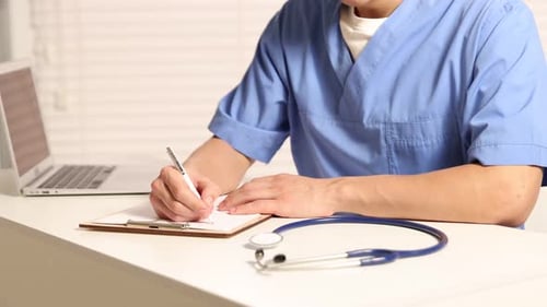 Medical Professional Writes on Clipboard in Exam Room