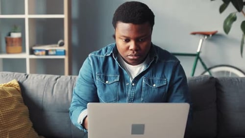 Focused man using laptop on couch at home