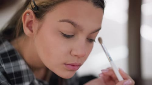 Junges Mädchen verwendet Make-up-Pinsel, um Make-up unter den Augen in Nahaufnahme zu mischen