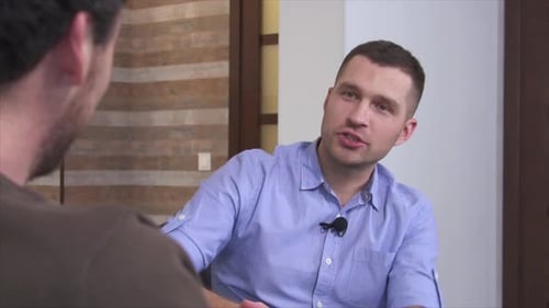 Emotionaler, fröhlicher positiver junger Mann oder Interviewer oder Blogger, der mit einem anderen Mann im Zimmer spricht