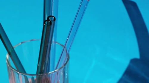 Juego de pajitas de vidrio reutilizables en vidrio con agua sobre fondo azul, ecológicas, con