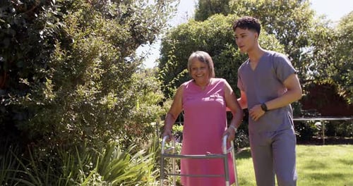 Helping senior woman with walker, male physiotherapist providing support outdoors