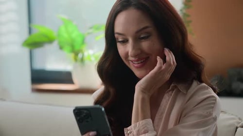 Woman Smiles Using Smartphone in Living Room