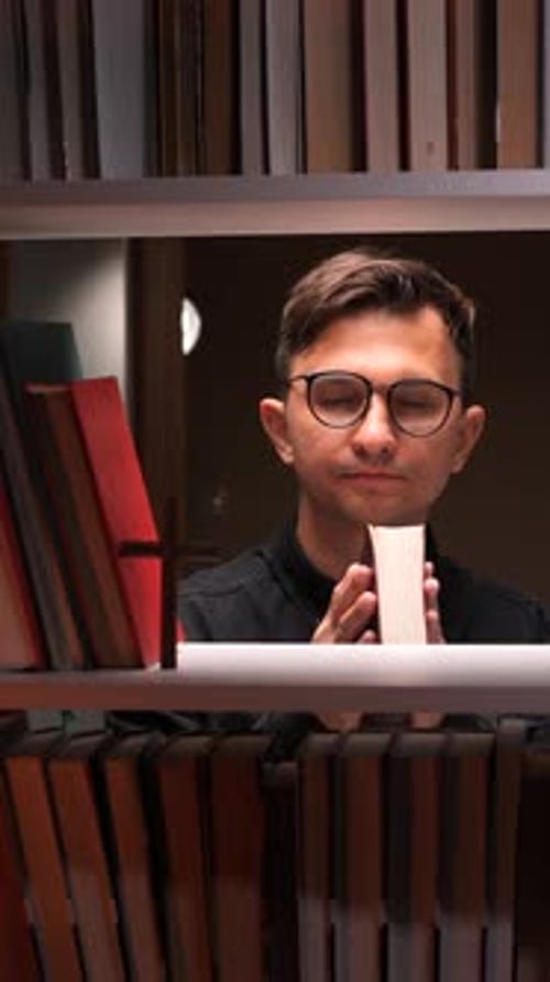 Vertical Video Priest Praying with Holy Bible in Library with Bookshelves and Cross