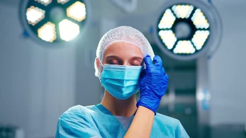 Close-up portrait of a girl surgeon in uniform in the operating room takes off medical mask from her