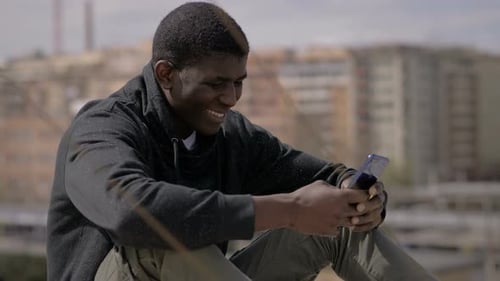 smiling happy young black african man using smartphone on Building roof