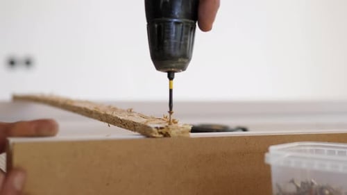 Gros plan à la main à l'aide d'une perceuse électrique pour percer un trou précis dans le bord du carton lors du montage à faire soi-même